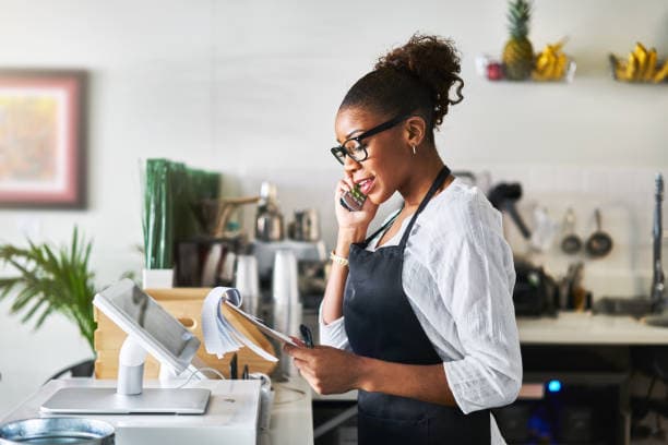 A cashier talking to a customer via the phone and looking at a notepad.